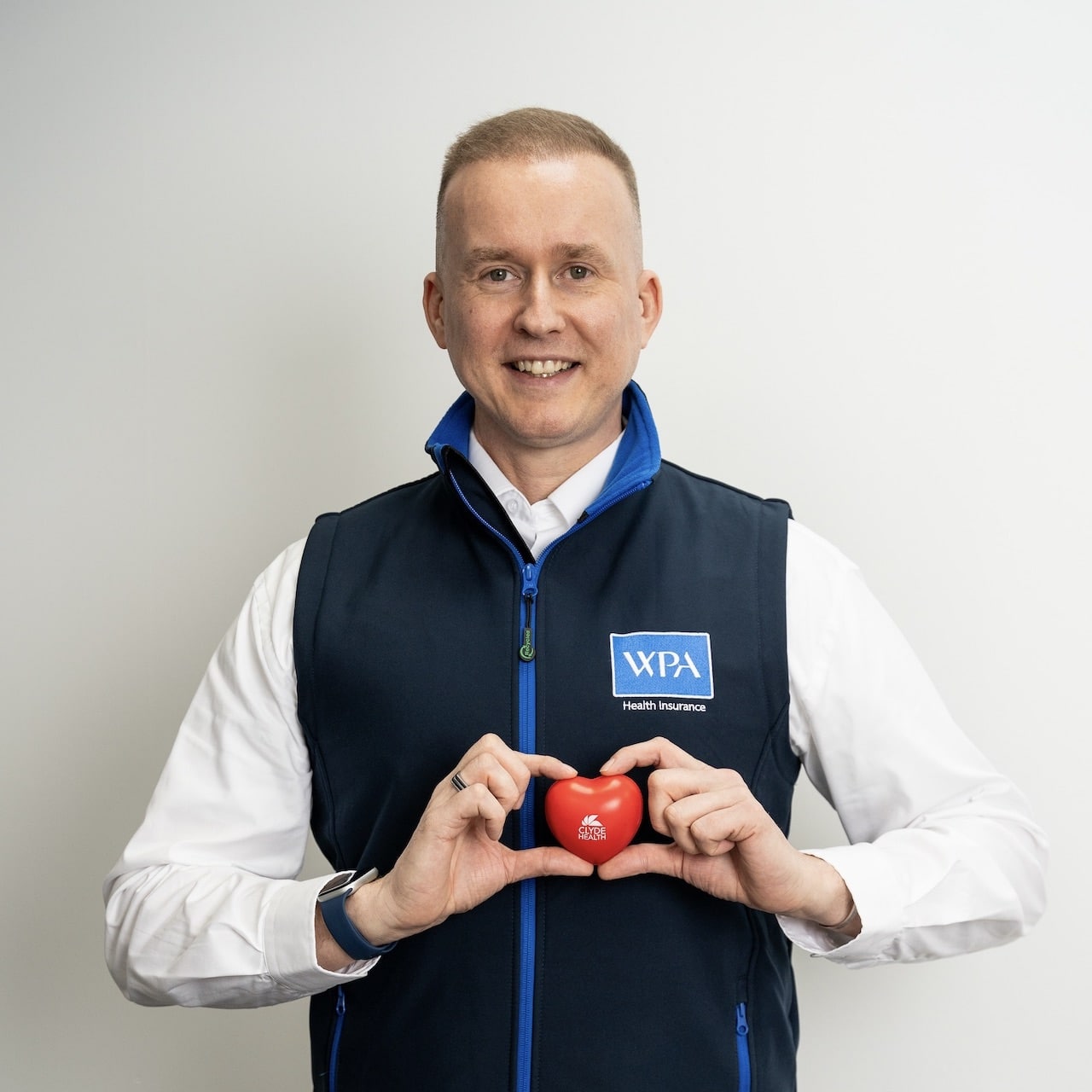 A man holds up a model heart in front of his chest with the words Clyde Health written on it